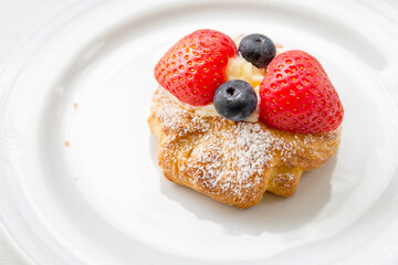 Close up of Danish Pastry Fresh Fruit, Fresh croissant with whipped cream and strawberries blueberries on a white plate