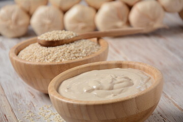 Tahini and sesame seeds in wooden bowls on wooden table.