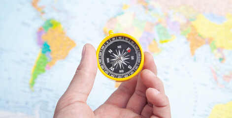 Male hand showing compass on the world map background.