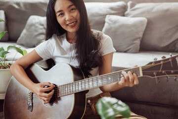 Woman playing guitar at home. Beautiful woman smiling and playing guitar with her plants in living...