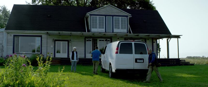 WIDE HANDHELD Two workers delivering package, bringing box from van to a house. White car with copy space. Shot with 2x anamorphic lens