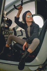 Tween girl in mirrored sunglasses sitting on pilots seat in open helicopter