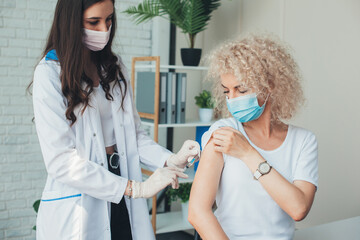 Side view photo of a blonde curly woman having a corona virus vaccine at the medical center from a...
