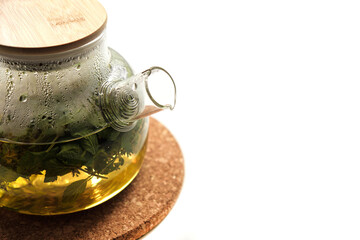 Misted glass teapot with a spring on a cork stand on a white background. Close-up - a spring in a teapot spout.