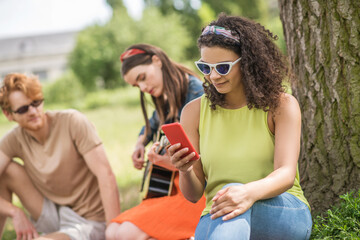 Girl looking into smartphone girlfriend with guitar and boyfriend
