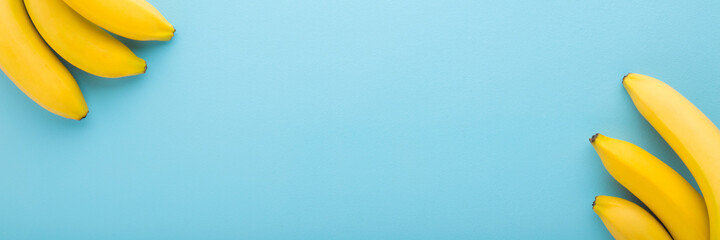 Beautiful fresh yellow bananas on light blue table background. Pastel color. Closeup. Fruits wide banner. Empty place for text. Top down view.