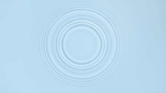 White drop falls down creating circles on water surface on pale blue background | Background shot for skin care cosmetics commercial