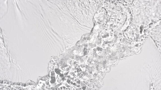 Water flows from opposite sides creating waves, ripples and concentric circles on pale grey background | Background shot for skin care cosmetics with hyaluronic acid commercial