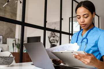 Black woman doctor working with laptop and papers at home