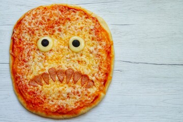 Halloween scary monster face pizza made from pizza dough,pizza sauce,mozzarella cheeses,sausage and...