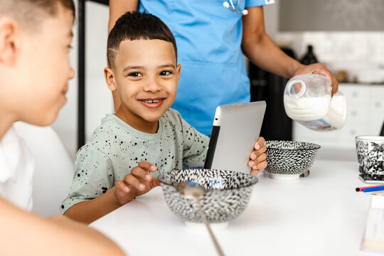 Two boys using tablet computer while having breakfast at home