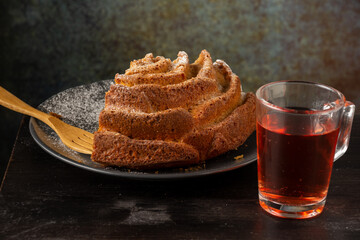 Top view of yogurt sponge cake on dark plate with sugar and wooden fork and glass cup with rooibos tea, selective focus, on wooden table and gray background, horizontal
