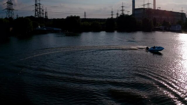 Motor boat on water at sunset. Panoramic view of the evening river with boat. Motor boat driving at the water surface and leaving a trace. View from above