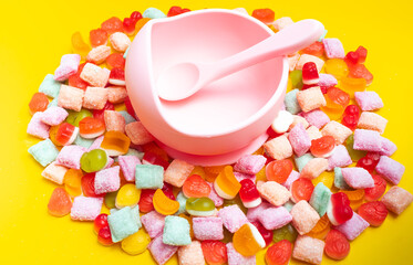 Children's tableware silicone bowl with spoon. Serving baby food, kid dishware.Pink silicone bowl and spoon are in a heap of sweets and marmalade. bright, colorful photo