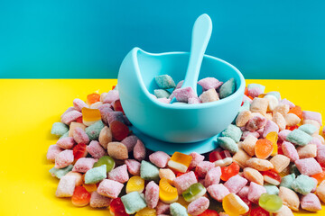 Children's tableware silicone bowl with spoon. Serving baby food, kid dishware.blue silicone bowl and spoon are in a heap of sweets and marmalade. bright, colorful photo