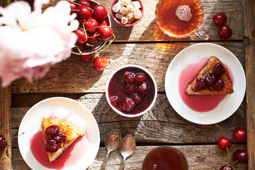 Cherry pie with jam in a bowl. Tea, flowers. Wooden background, top view