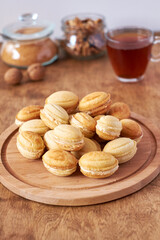 Walnut cookies with cream filling. Cookies on a wooden board. Side view, white and wood background. Tea.