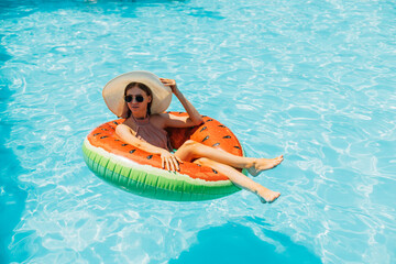 Happy beautiful young woman in sunglasses bathing on an inflatable big donut in the pool, summer vacation concept