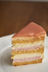 a piece of cake on a plate. White chocolate sponge cake, strawberry cheesecake and white mousse. Top with strawberry frosting.