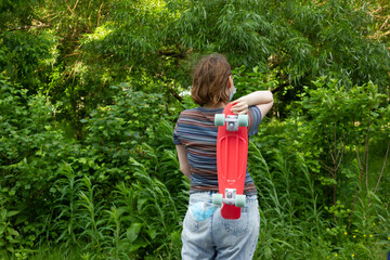 close up stylish girl carrying the penny board on the background of green trees