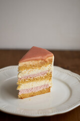 a piece of cake on a plate. White chocolate sponge cake, strawberry cheesecake and white mousse. Top with strawberry frosting.