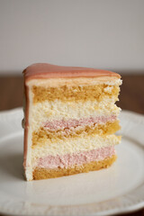 a piece of cake on a plate. White chocolate sponge cake, strawberry cheesecake and white mousse. Top with strawberry frosting.