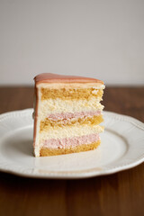 a piece of cake on a plate. White chocolate sponge cake, strawberry cheesecake and white mousse. Top with strawberry frosting.