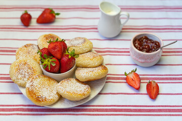 Syrniki or cottage cheese fritters with strawberry jam on a white plate. 