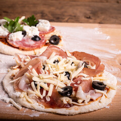 Cooking mini pizza - mini pizza with ham, olives and mozzarella cheese, close-up