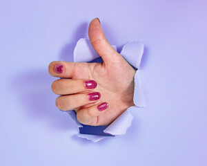 Woman hand in whole of torn purple paper background