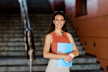 A young student in casual clothes with an essay in a folder and a phone in her hands