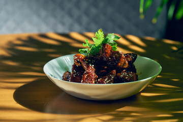 Pork ribs in sweet and sour sauce with cilantro, sesame seeds and Sichuan pepper in a white bowl. Chinese cuisine