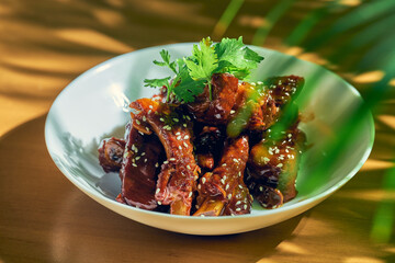 Pork ribs in sweet and sour sauce with cilantro, sesame seeds and Sichuan pepper in a white bowl. Chinese cuisine