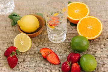 Fototapeta na wymiar A tall glass cup of water with ice. Sliced oranges, lemons, lime and strawberry