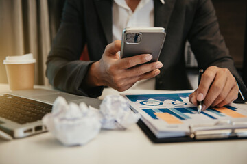 Fototapeta premium Business man working at office with smartphone and laptop and documents on his desk, financial adviser analyzing data.
