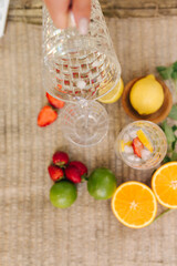 Top view of two tall glasses with water ice and strawberry. Slices fresh fruits on the table outdoor. Lime lemon and orange. Food concept. Woman pouring water