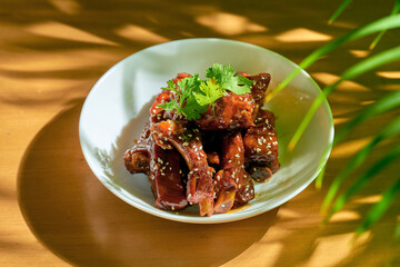 Pork ribs in sweet and sour sauce with cilantro, sesame seeds and Sichuan pepper in a white bowl. Chinese cuisine