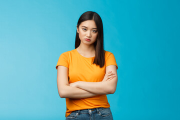 Serious-looking indifferent and upset intense asian woman brunette, cross arms chest look strict ignorant, pissed listening nonsense, annoyed stupid conversation, stand blue background - obrazy, fototapety, plakaty