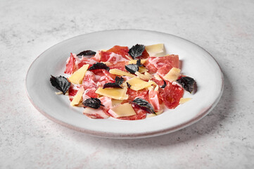 Close up prosciutto coppa di parma ham slices with parmesan cheese and dark basil on light plate on textured background