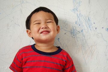Cute smiling Asian boy wearing a bright red striped T-shirt standing on white background. with text copy space, Selective focus
