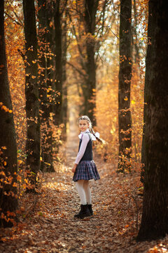 Cute schoolgirl in school uniform turns around in the autumn forest
