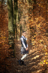 Cute schoolgirl in a school uniform on a forest path in an autumn forest
