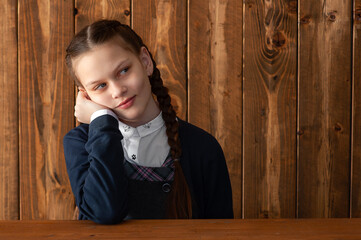 Cute smiling schoolgirl in uniform sitting at her desk on wooden background