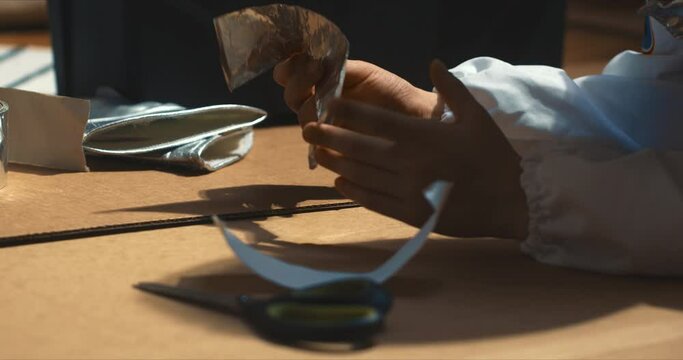 Close-up hands of little child having fun building, sticking big cardboard pieces with silver scotch tape and scissors.