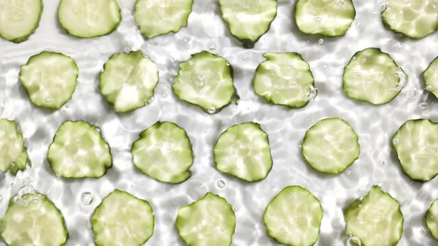 Multiple waves of water cross each other creating ripples and bubbles spontaneously on cucumber background | Skincare cosmetics background shot for commercial