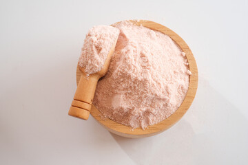 Top view of Himalayan pink salt powder in wooden bowl and scoop isolated on white background. 