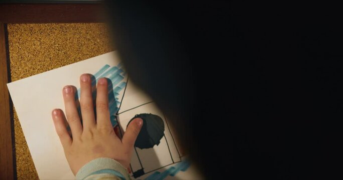 Dreams about future. Close-up hands of creative boy child put drawing sheet with space rocket art on cork pin board.
