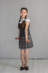 Cute smiling school girl in uniform standing on a gray background