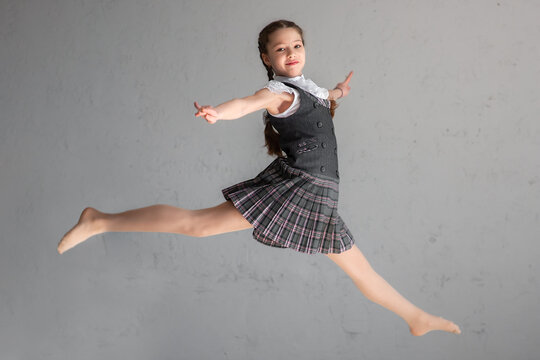 Cute smiling schoolgirl in uniform jumping on gray background