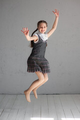 Cute smiling schoolgirl in uniform jumping on gray background - obrazy, fototapety, plakaty